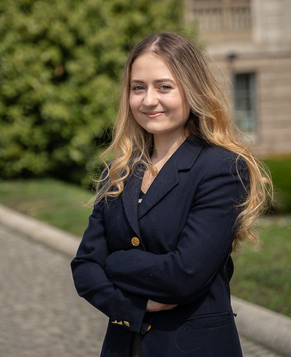 Kobieta w eleganckiej marynarce stoi na brukowanej drodze.